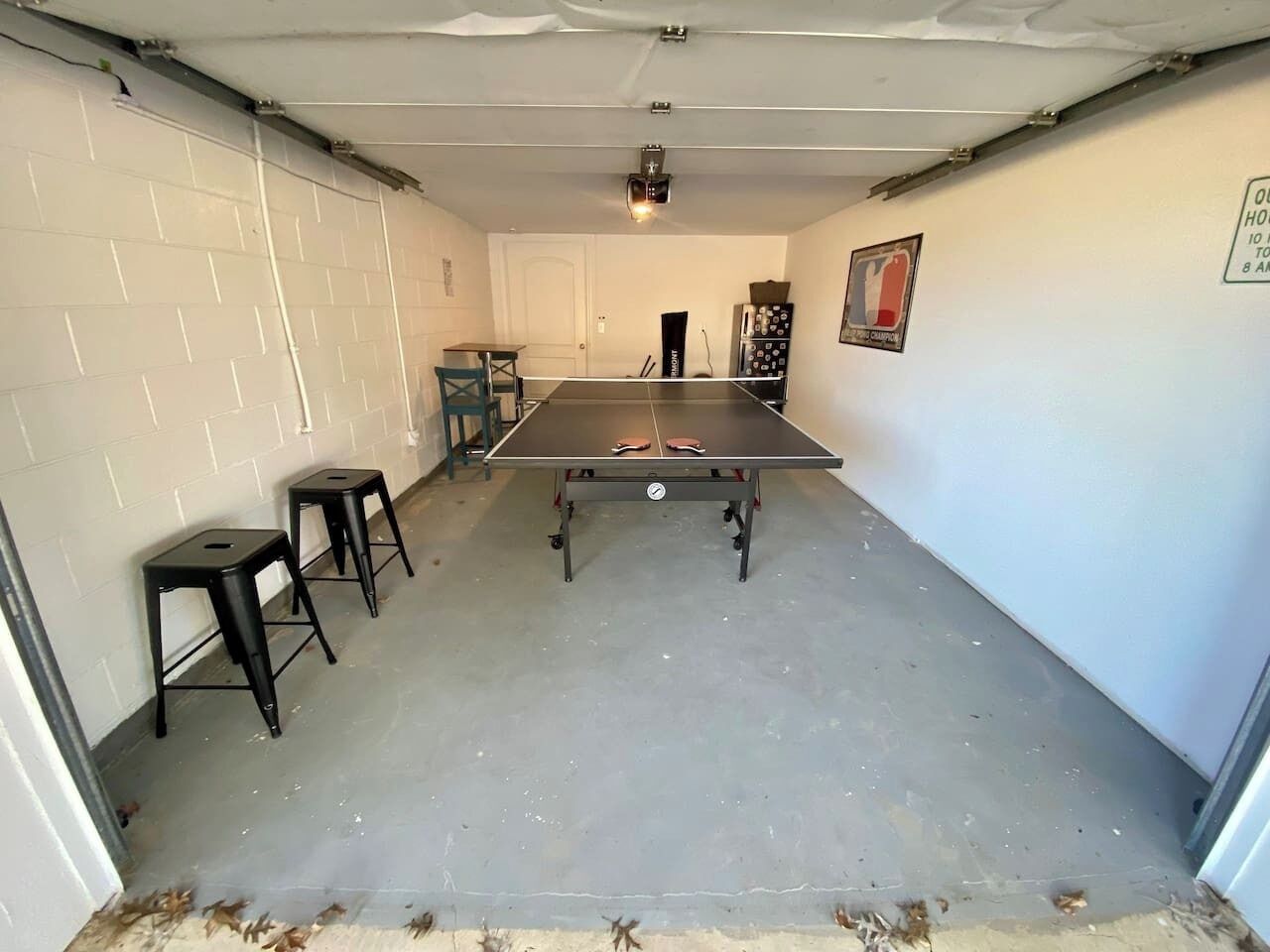 A garage with a ping pong table, two stools, and a door.
