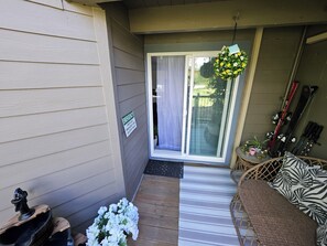 A covered patio area with a sliding glass door, a small seating area with a patterned cushion, and a sign indicating emergency services. - Lovely 2-bedroom apartment in Silverthorne with fitness clubhouse (Silverthorne)