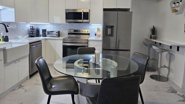 A modern kitchen with white cabinets, stainless steel appliances, a glass dining table, and black chairs.