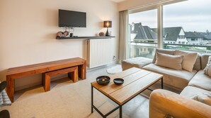A modern living room with a wooden bench, a sofa, a coffee table, and a TV mounted on the wall.