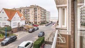 A coastal residential area with multi-story buildings, a street with parked cars, and a view of the beach.