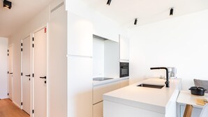 A modern kitchen with white cabinetry, a built-in oven, and a coffee maker. - Newly built flat with sea view (Koksijde)