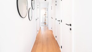 A hallway with white walls and wooden flooring, leading to a room with a door and a ladder. - Newly built flat with sea view (Koksijde)