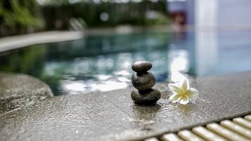 Un tas de pierres avec une fleur blanche à côté d’une piscine.