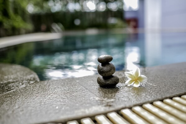 A stone stack with a white flower beside a pool. - Apartement Gunung Putri Square WhiteBox (Gunung Putri)