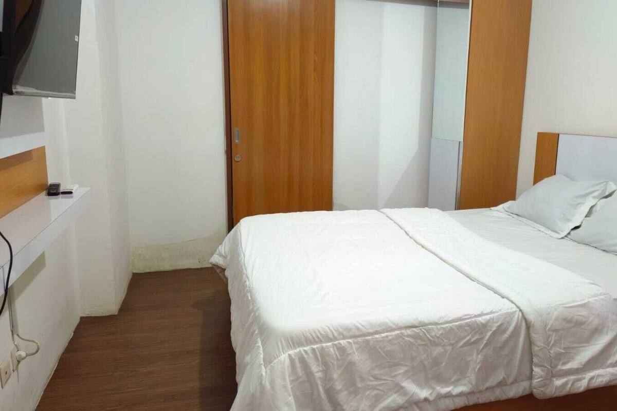 A bedroom with a bed, wooden wardrobe, and a mirror.