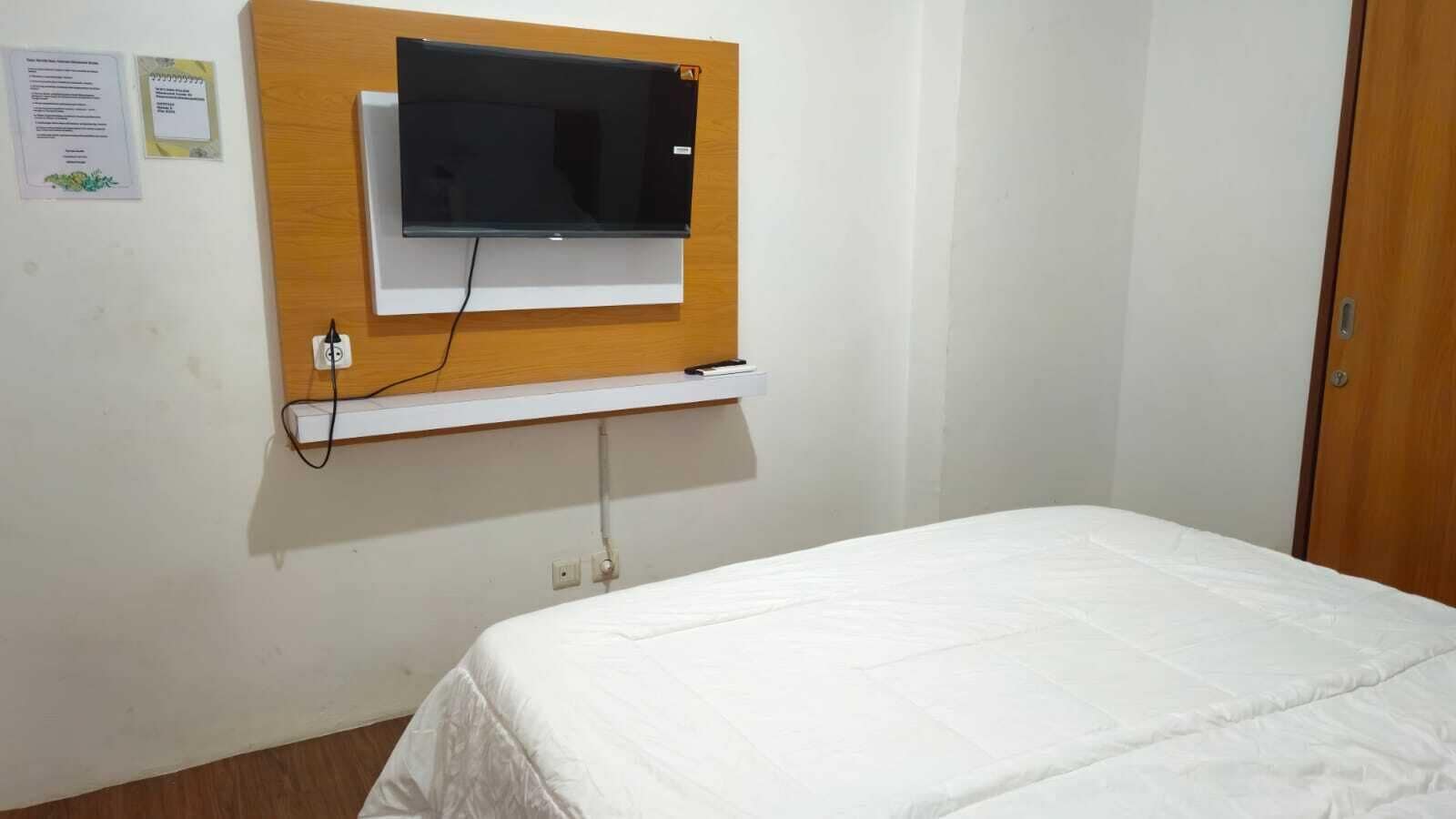 A bedroom with a bed, a mounted TV, and a wooden shelf.