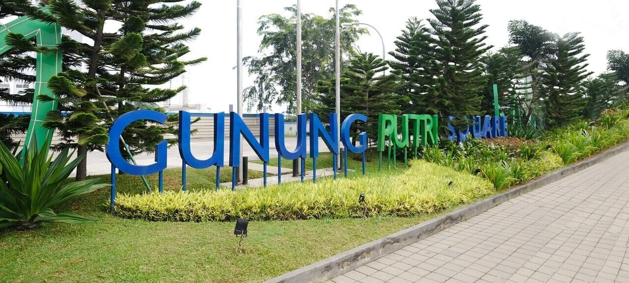 A sign for Guingung Puteri Square with a paved walkway and greenery.