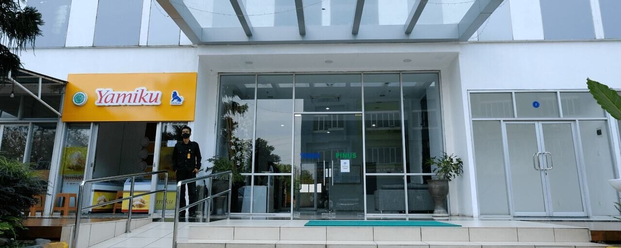 Un bâtiment moderne avec une entrée en verre, une enseigne indiquant « Yamiku » et une rampe d’accès pour les personnes à mobilité réduite.