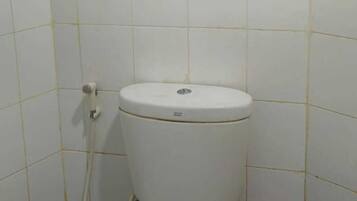 Une petite salle de bain simple, avec des toilettes, une tuyauterie apparente et des murs carrelés.