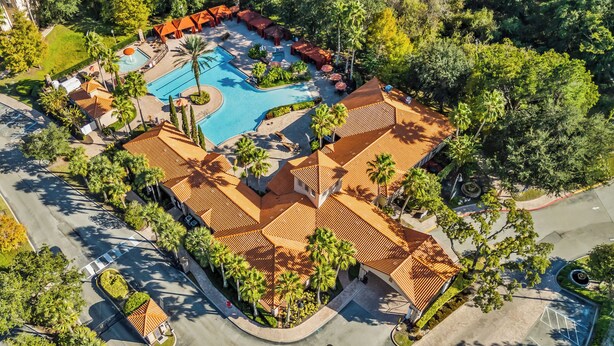 An aerial view of a resort with a swimming pool, palm trees, and a covered seating area.