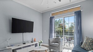 A modern living room with a flat-screen TV, grey sofa, and a glass door leading to an outdoor area.