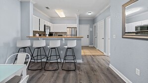 A modern kitchen with white cabinets, a central island with stools, and a large mirror on the wall.