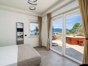 Ένα υπνοδωμάτιο με ένα κρεβάτι, ένα μεγάλο παράθυρο και θέα σε μια βεράντα με έπιπλα εξωτερικού χώρου.