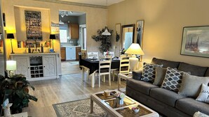 A living room with a sofa, a coffee table, and a dining area with a table and chairs. There is a kitchen in the background. - Cozy 2 bed 2 bath Santa Fe style, 55+ Senior Community Green Valley town home. (Green Valley)