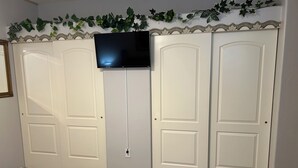 A bedroom with a bed, a TV mounted on the wall, and a wardrobe with a decorative vine. - Cozy 2 bed 2 bath Santa Fe style, 55+ Senior Community Green Valley town home. (Green Valley)