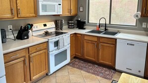A kitchen with wooden cabinets, a white microwave, a stove, a sink, and a dishwasher. - Cozy 2 bed 2 bath Santa Fe style, 55+ Senior Community Green Valley town home. (Green Valley)