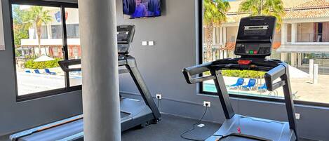 A gym with treadmills, a TV, and large windows overlooking a pool area.