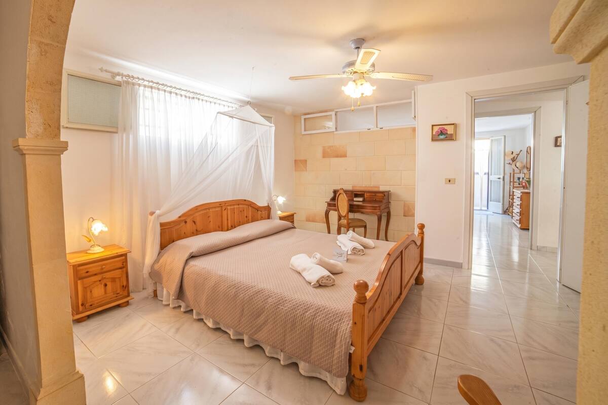 A bedroom with a bed, bedside lamps, a ceiling fan, a wooden nightstand, and a chair.