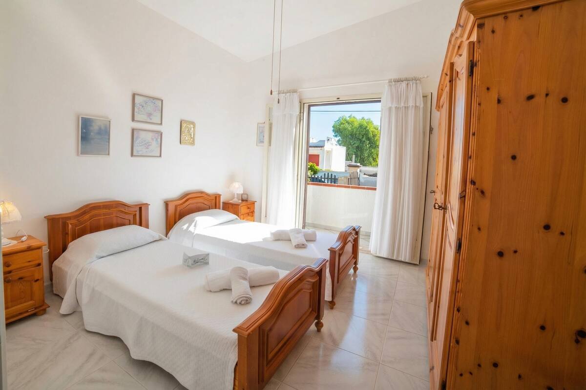A hotel room with two beds, a wooden wardrobe, a balcony with a view, and a tiled floor.