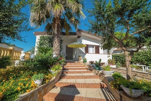 A house with a staircase leading to the entrance, surrounded by potted plants and flowers. - Villa Calò (Maruggio)
