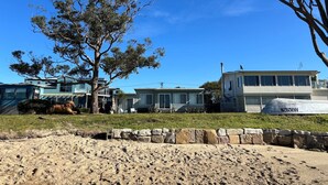 A beachfront property with multiple houses, a large tree, and a sandy foreground. - Noddy`s Charming Waterfront Cottage (Greenwell Point)