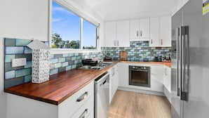 A modern kitchen with white cabinets, a wooden countertop, and a view of the outdoors through a large window. - Heated Pool, Fireplace, Games Room & Pet Friendly! (Sanctuary Point)