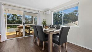 A dining area with a wooden table and chairs, large windows, and a view of the outdoors. - Heated Pool, Fireplace, Games Room & Pet Friendly! (Sanctuary Point)