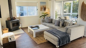 A cozy living room with a fireplace, a sofa set, and a large window. - Heated Pool, Fireplace, Games Room & Pet Friendly! (Sanctuary Point)