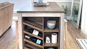 Una mesa de centro de madera con un soporte para vino, objetos decorativos y vista al océano.