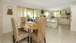 Una cocina moderna con armarios blancos, una isla central y un comedor con sillas de mimbre y una mesa de madera.