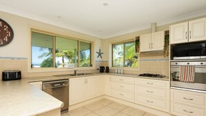 Una cocina moderna con armarios blancos, lavavajillas integrado, estufa y un ventanal con vistas a palmeras.