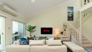 Una sala de estar moderna con un sofá modular, un televisor de pantalla plana y una escalera.