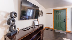 Un salon avec un téléviseur à écran plat fixé au mur, un meuble de rangement en bois sur lequel est posé un certificat encadré, et une porte verte.