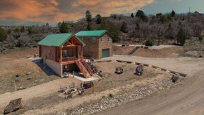 A two-story log cabin with a green roof, a balcony, and a front porch with outdoor seating. - National Parks - Cozy stay and UFO Sightings (Alton)