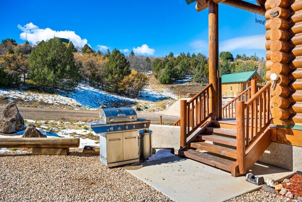 A wooden cabin with a barbecue grill and a portable stove on a gravel patio.