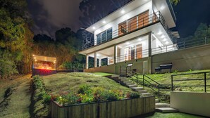 Et moderne hus med to etager, velbelyst facade, trappe til indgangen og en anlagt have med farverige blomster.