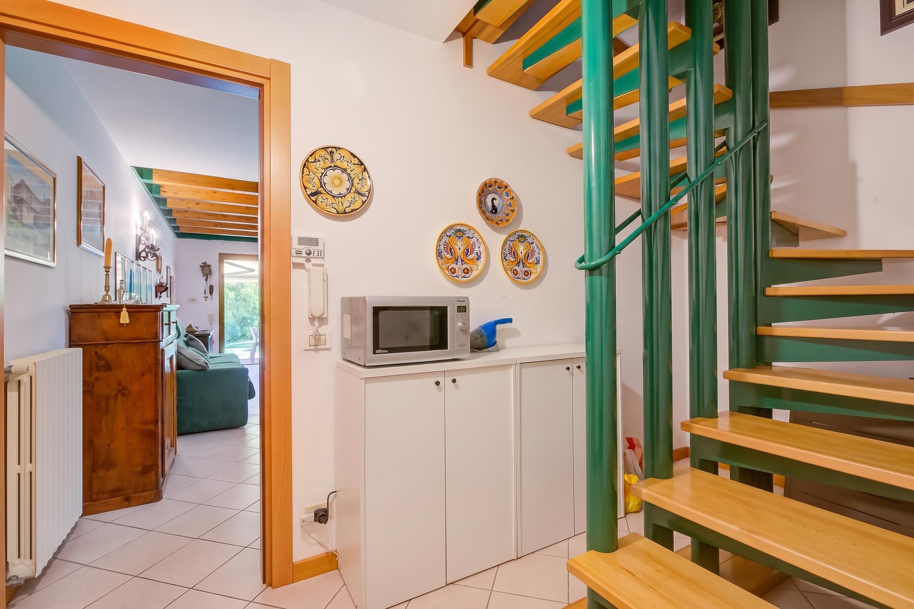 A staircase with green railings leading to a landing with a microwave and decorative plates.