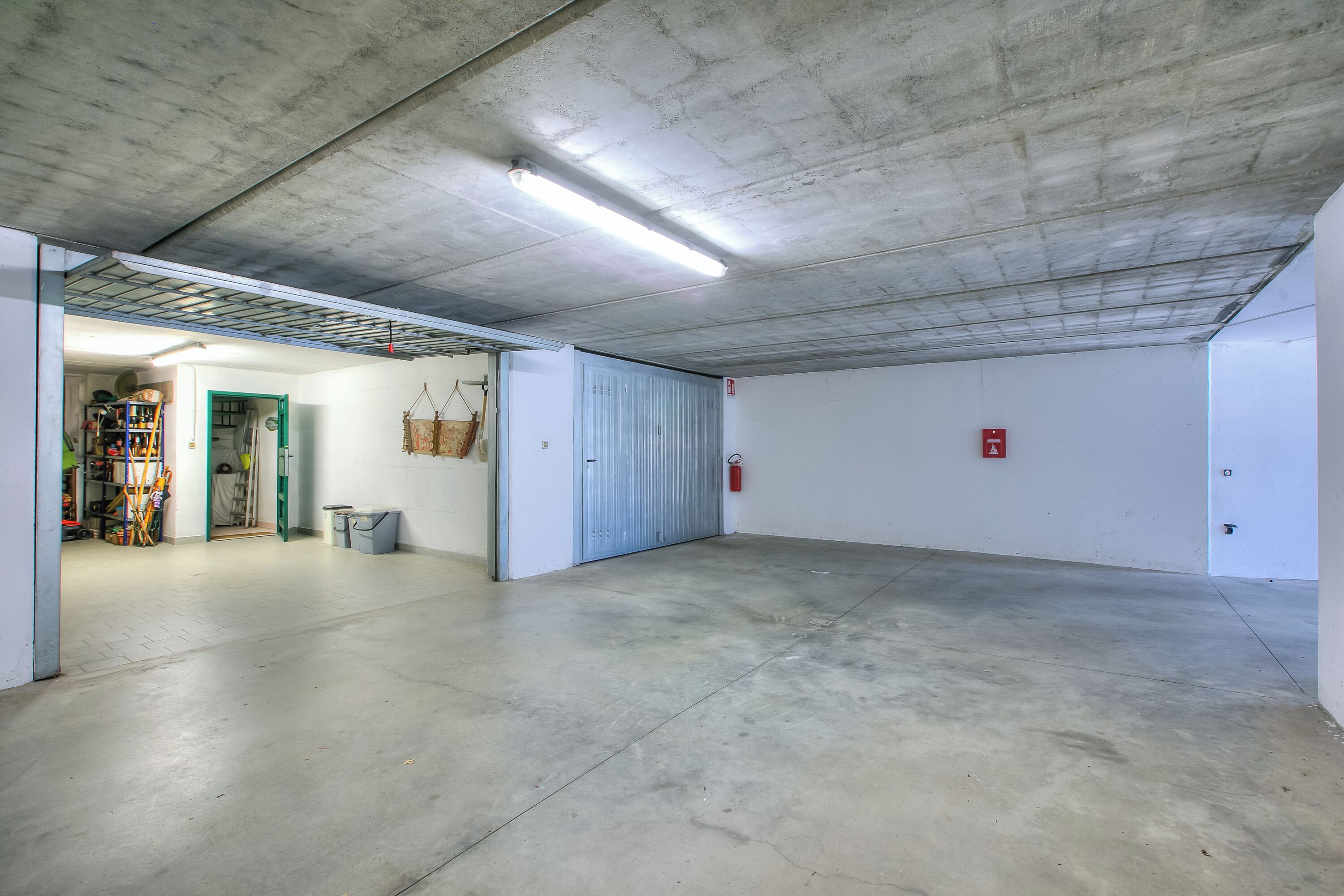 A spacious indoor area with a concrete floor and ceiling, a door leading to another room, and a fire extinguisher mounted on the wall.