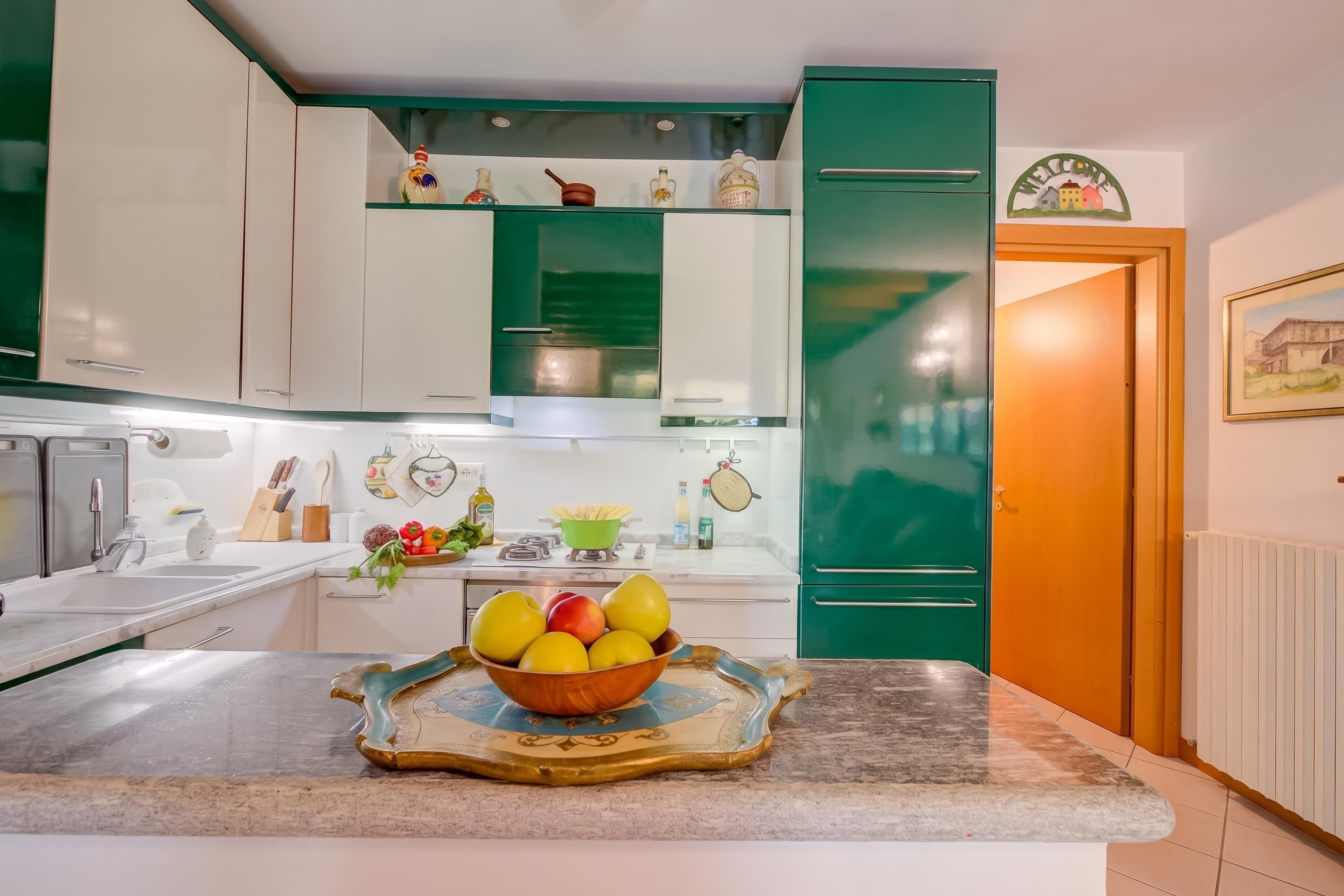 A kitchen with white and green cabinets, a fruit bowl on the counter, and a green refrigerator.