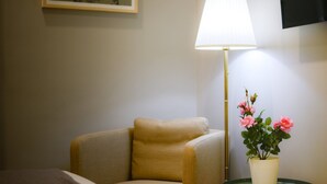 Een hotelkamer met een bed, een beige fauteuil, een vloerlamp en een tafeltje met een bloempot.