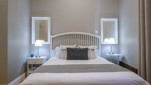 Une chambre à coucher bien rangée, avec un lit, deux tables de chevet, deux lampes et deux miroirs accrochés aux murs.