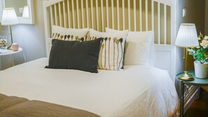 A neatly made bed with white bedding and a variety of pillows, including a dark gray one. There is a bedside table with a lamp and a small potted plant. - GuestReady - Casa Conforto & Chiado - Room 11 (Ponta Delgada)