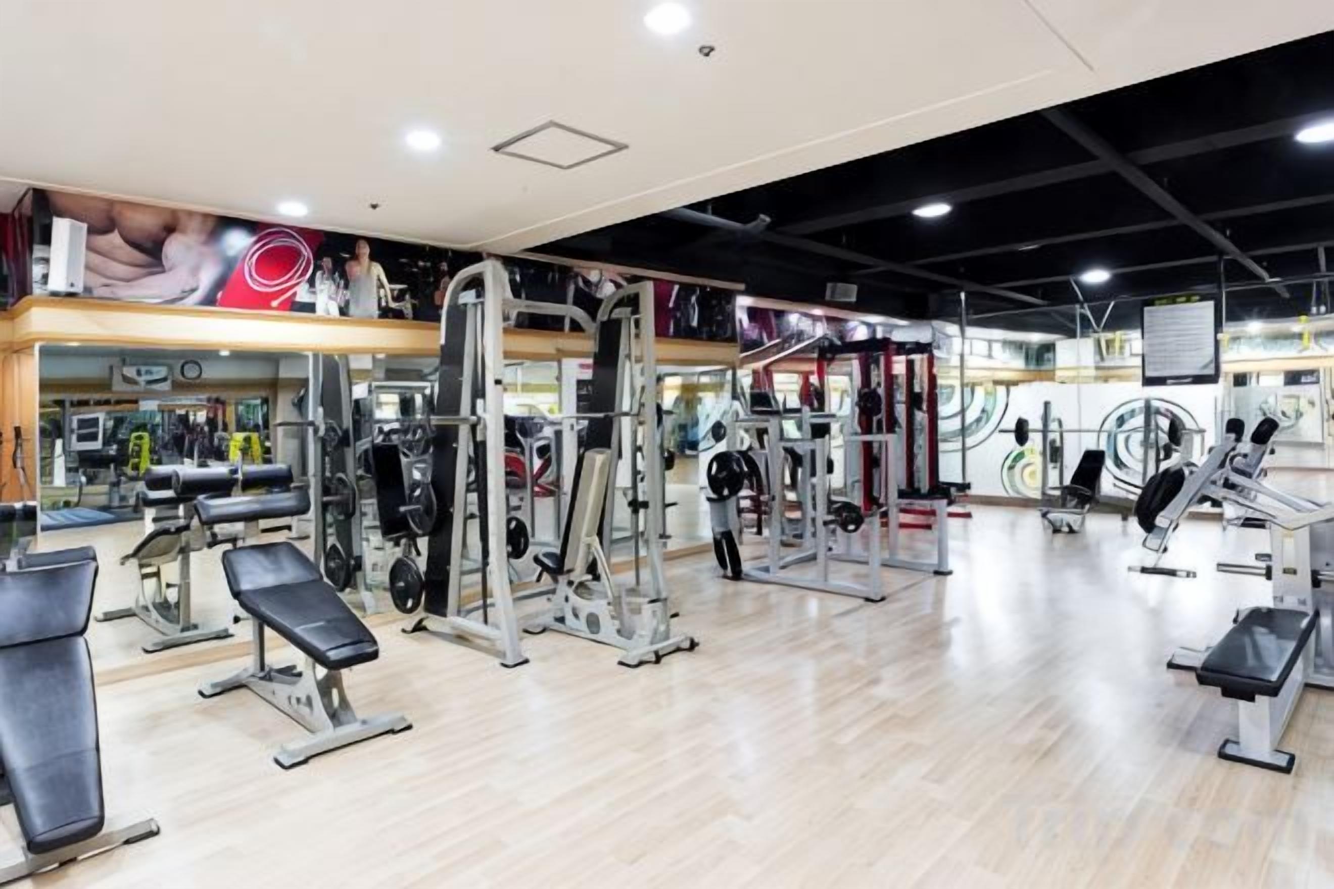 Ein Fitnessstudio mit unterschiedlichen Trainingsgeräten, einer Spiegelwand und einem Holzboden.