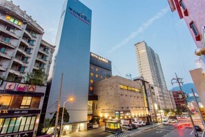 A modern hotel with a prominent vertical sign, adjacent buildings, and a street with vehicles. - Lamer Hotel & Seawater Spa Busan (Busan)