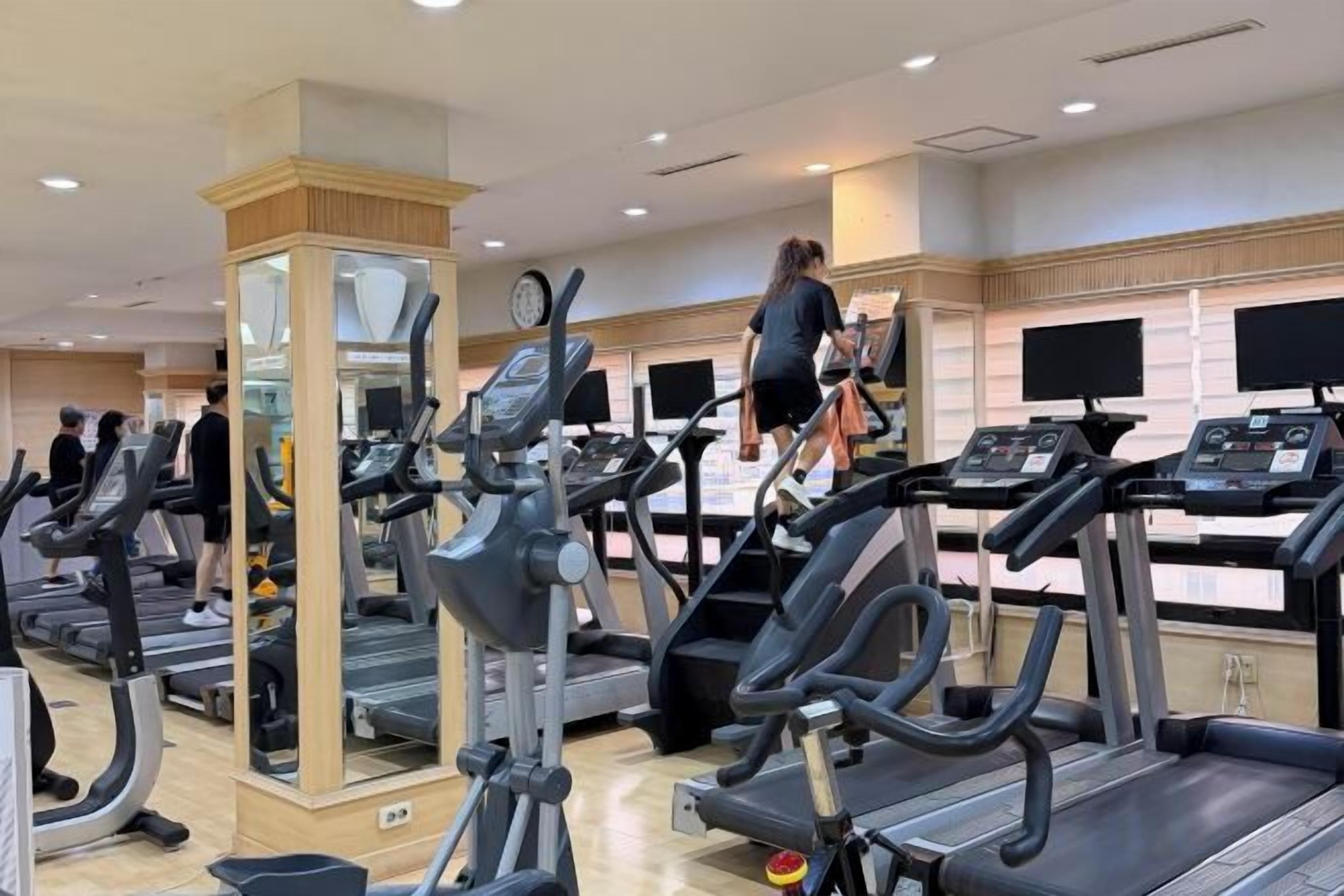 A gym with multiple treadmills, a mirrored column, and a person using a treadmill.