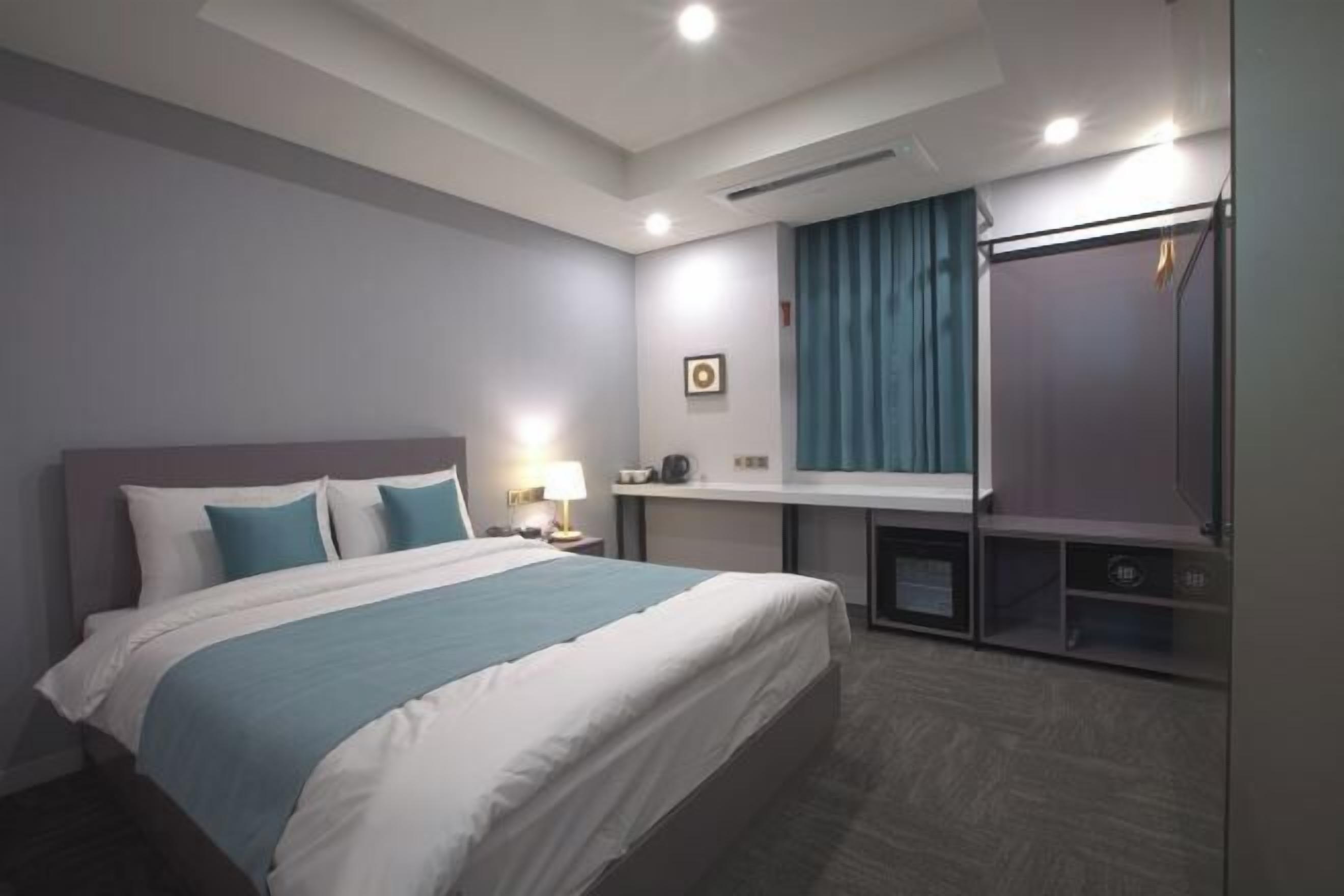 Una habitación de hotel con cama, mesita de noche, lámpara y espejo.