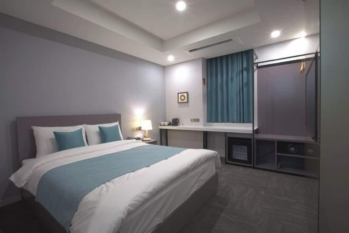 Una habitación de hotel con cama, mesita de noche, lámpara y espejo.