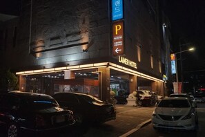 Entrada de un hotel con un letrero de estacionamiento, acceso cubierto y varios coches aparcados.