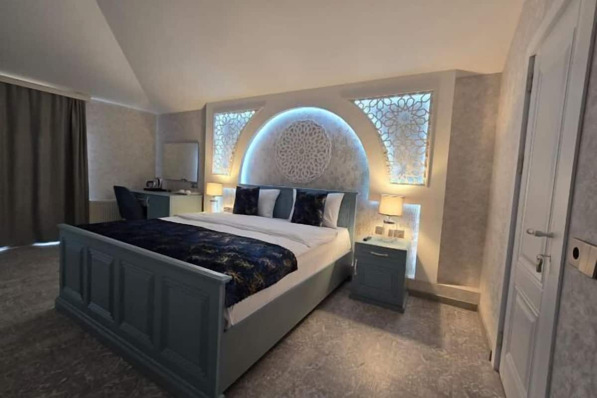 A bedroom with a bed, bedside tables, a mirror, and a window with a decorative light.